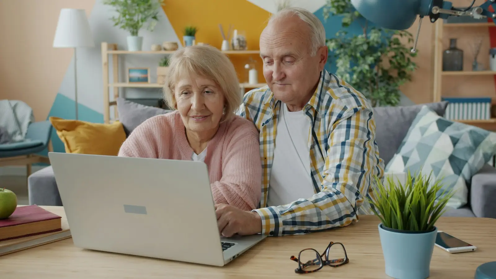 Ein älteres Paar sitzt zu Hause gemeinsam vor einem Laptop.